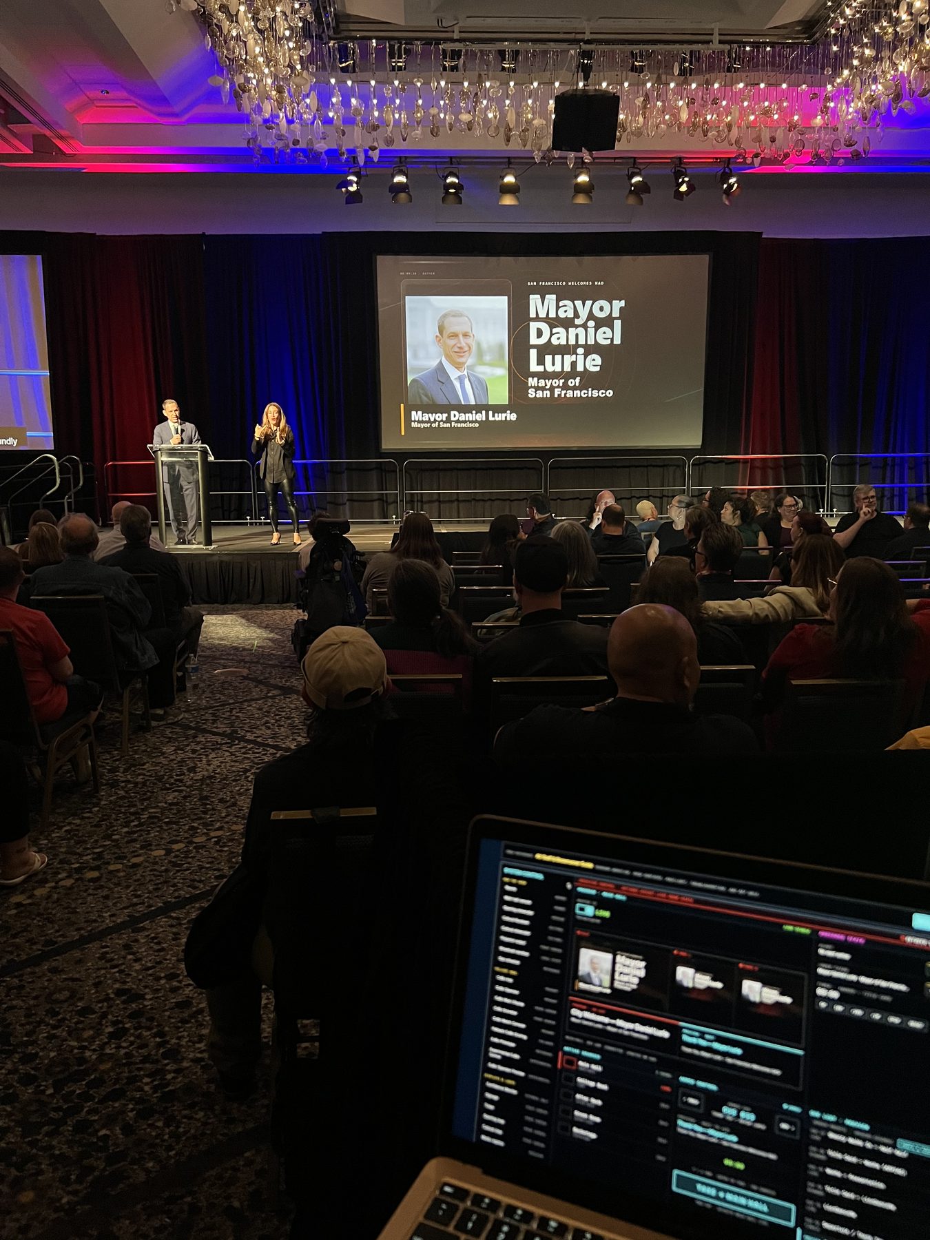 The main ballroom screen displaying a speaker identity graphic for Mayor Daniel Lurie, Mayor of San Francisco, with a lower-third title, viewed from the operator position.